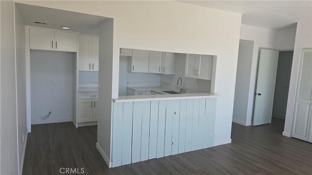 kitchen with kitchen peninsula, dark hardwood / wood-style flooring, white cabinetry, and sink