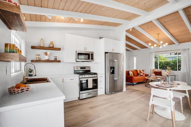 kitchen featuring appliances with stainless steel finishes, vaulted ceiling with beams, white cabinetry, and sink