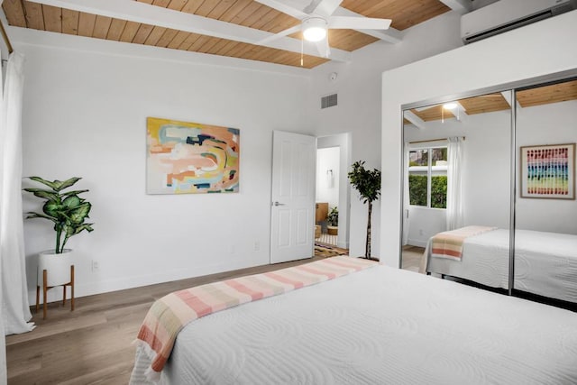 bedroom featuring beam ceiling, ceiling fan, an AC wall unit, hardwood / wood-style floors, and a closet