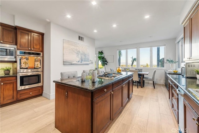 kitchen featuring dark stone counters, a center island, appliances with stainless steel finishes, and light hardwood / wood-style flooring