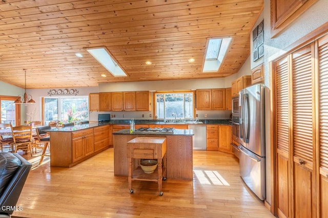 kitchen featuring a center island, lofted ceiling with skylight, appliances with stainless steel finishes, light hardwood / wood-style floors, and a kitchen bar