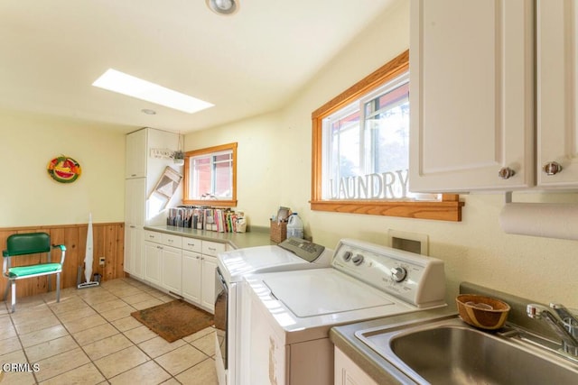 clothes washing area with cabinets, sink, light tile patterned floors, washing machine and dryer, and wood walls