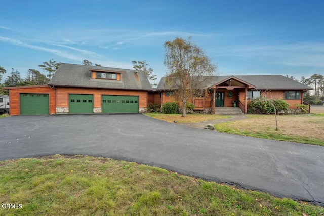 view of front of home featuring a front lawn, stone siding, a garage, and aphalt driveway