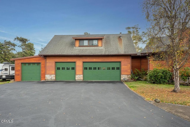 view of front facade with roof with shingles, stone siding, and a detached garage