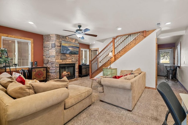 carpeted living room featuring a stone fireplace and ceiling fan