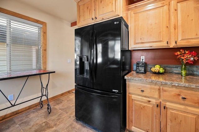 kitchen featuring light brown cabinets, light stone countertops, and black refrigerator with ice dispenser