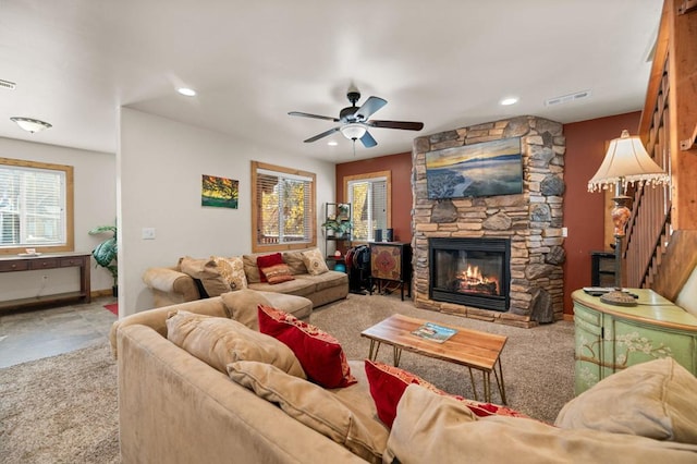 living room with a stone fireplace, ceiling fan, and light colored carpet