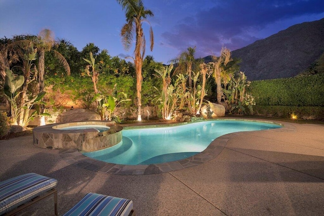 pool at dusk featuring an in ground hot tub, a mountain view, and a patio