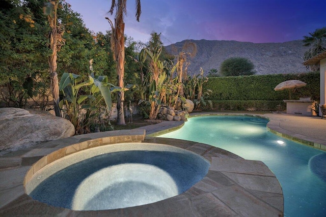 pool at dusk with a mountain view and an in ground hot tub