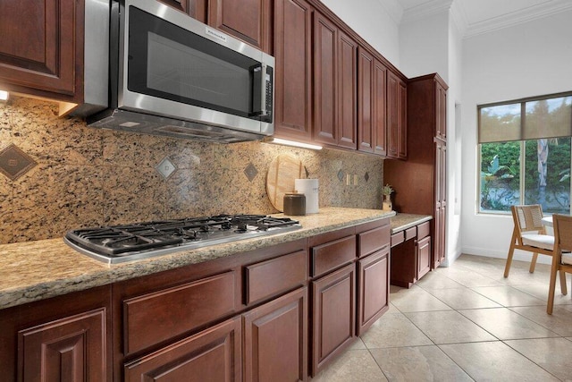 kitchen with light stone counters, appliances with stainless steel finishes, decorative backsplash, light tile patterned flooring, and ornamental molding