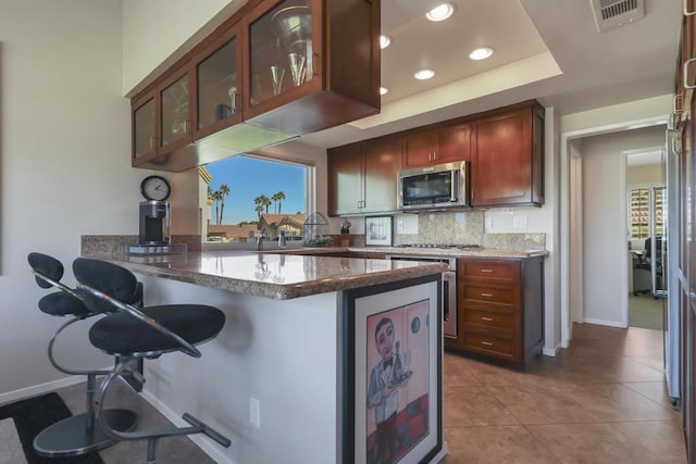 kitchen with tasteful backsplash, kitchen peninsula, dark stone countertops, a breakfast bar area, and light tile patterned floors