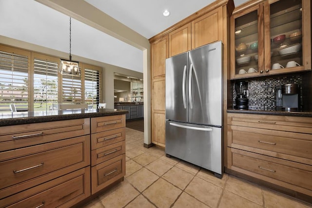 kitchen featuring backsplash, dark stone counters, decorative light fixtures, light tile patterned flooring, and stainless steel refrigerator