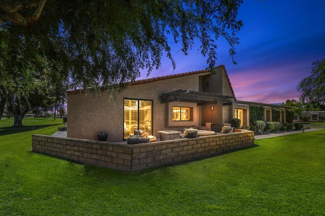 back house at dusk featuring a pergola and a yard