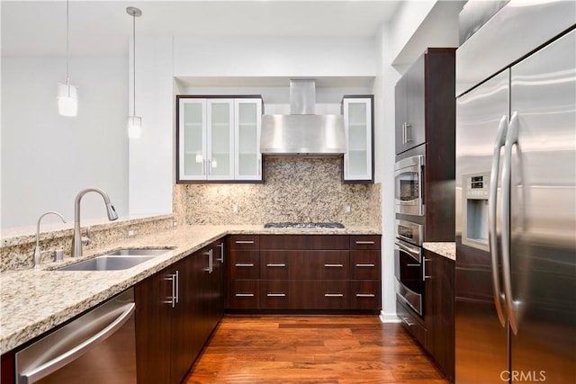 kitchen featuring dark wood-type flooring, wall chimney range hood, sink, built in appliances, and decorative light fixtures