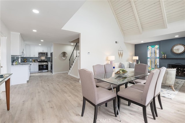 dining area featuring lofted ceiling with beams, sink, light hardwood / wood-style floors, and wooden ceiling