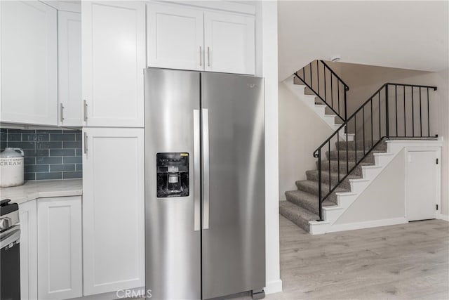 kitchen featuring light wood-type flooring, stainless steel appliances, decorative backsplash, and white cabinetry