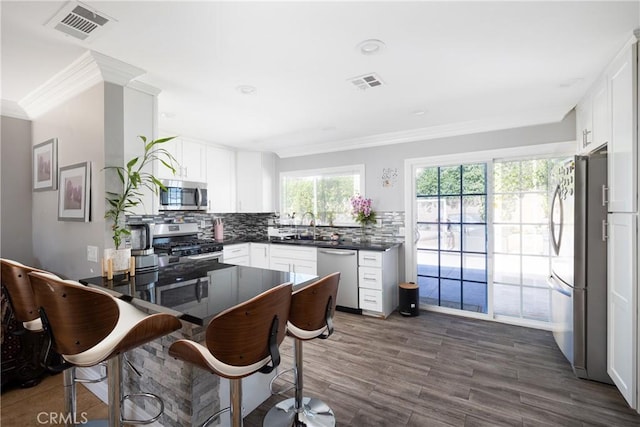 kitchen with dark wood-type flooring, white cabinets, ornamental molding, appliances with stainless steel finishes, and tasteful backsplash