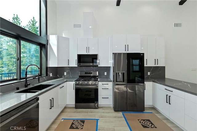 kitchen with backsplash, a towering ceiling, sink, stainless steel appliances, and white cabinets