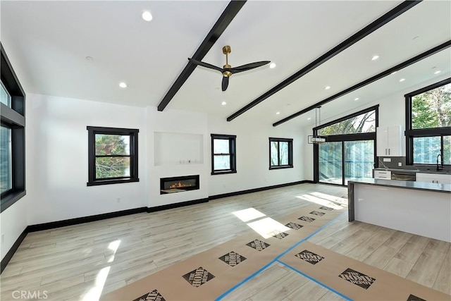 unfurnished living room featuring ceiling fan, vaulted ceiling with beams, and sink