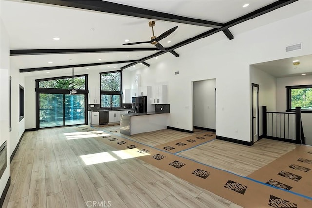 unfurnished living room with light wood-type flooring, ceiling fan, a healthy amount of sunlight, and beamed ceiling