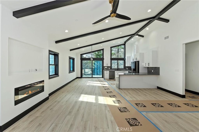 unfurnished living room with ceiling fan, vaulted ceiling with beams, and light hardwood / wood-style flooring