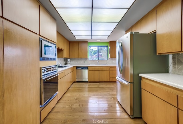 kitchen featuring light wood-type flooring, stainless steel appliances, backsplash, and sink