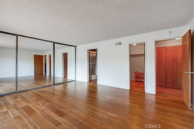 unfurnished bedroom with hardwood / wood-style floors, a spacious closet, and a textured ceiling