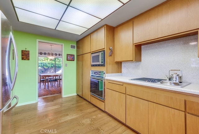 kitchen featuring light brown cabinets, light wood-type flooring, stainless steel appliances, and tasteful backsplash