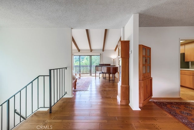 hallway with hardwood / wood-style floors, lofted ceiling with beams, and a textured ceiling