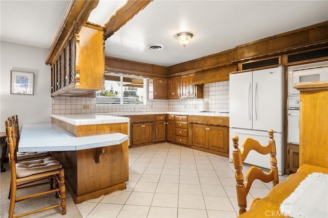 kitchen with white fridge, tasteful backsplash, kitchen peninsula, light tile patterned flooring, and a breakfast bar area