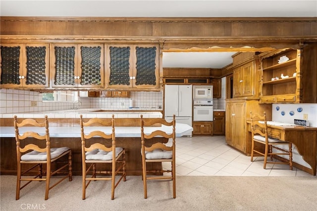 kitchen featuring tile countertops, a kitchen bar, kitchen peninsula, white appliances, and light tile patterned floors