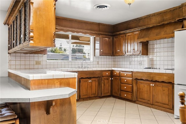 kitchen with white refrigerator, tasteful backsplash, kitchen peninsula, a breakfast bar, and light tile patterned floors