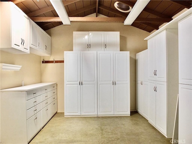 interior space featuring light colored carpet, wooden ceiling, white cabinets, and lofted ceiling with beams