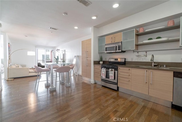 kitchen with sink, a kitchen breakfast bar, dark hardwood / wood-style floors, light brown cabinetry, and appliances with stainless steel finishes