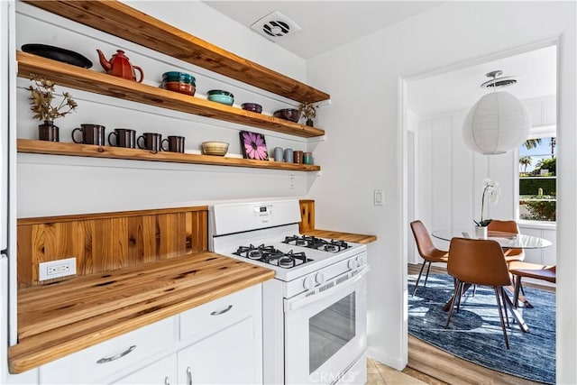 kitchen featuring white gas range, white cabinetry, wood counters, light hardwood / wood-style flooring, and pendant lighting