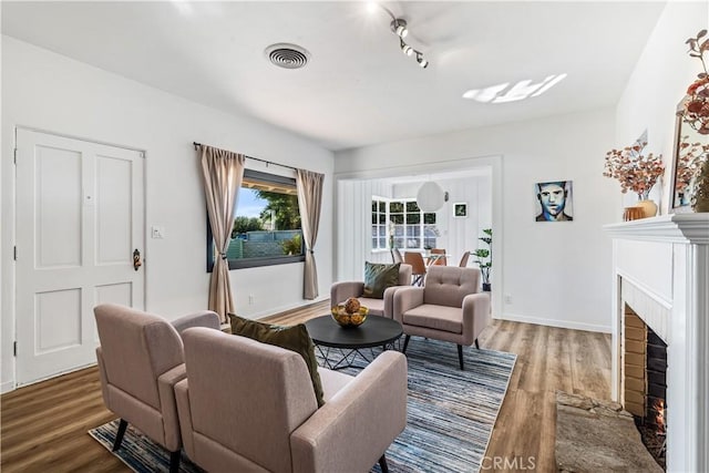 living room with wood-type flooring, track lighting, and a brick fireplace