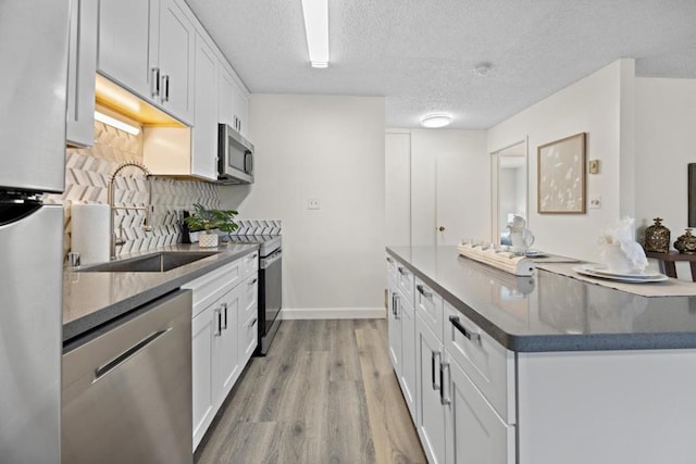 kitchen featuring sink, light wood-type flooring, a textured ceiling, appliances with stainless steel finishes, and white cabinetry