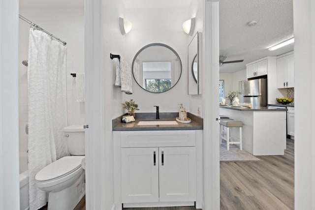 full bathroom with ceiling fan, wood-type flooring, a textured ceiling, toilet, and vanity