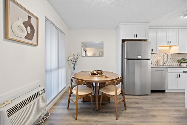 dining room featuring a wall mounted air conditioner, a textured ceiling, and light hardwood / wood-style flooring