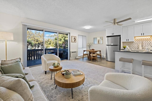 living room with a textured ceiling, light wood-type flooring, an AC wall unit, and ceiling fan