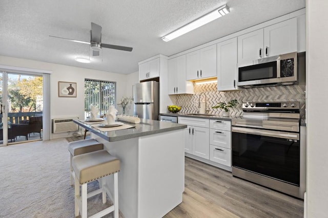 kitchen with white cabinetry, sink, a center island, stainless steel appliances, and a kitchen bar