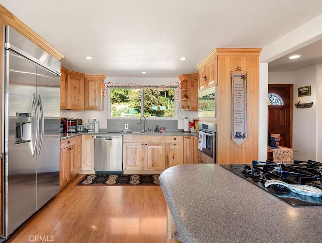 kitchen featuring built in appliances, sink, light brown cabinetry, and light wood-type flooring