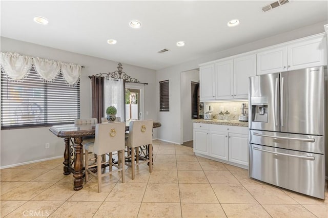 kitchen featuring white cabinetry, light stone counters, backsplash, stainless steel fridge, and light tile patterned flooring