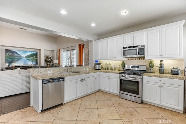 kitchen with backsplash, white cabinets, sink, appliances with stainless steel finishes, and kitchen peninsula