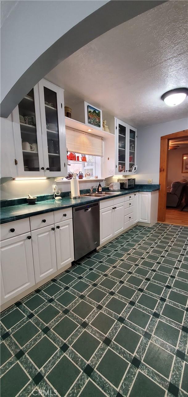 kitchen featuring dishwasher, dark countertops, dark floors, glass insert cabinets, and white cabinetry