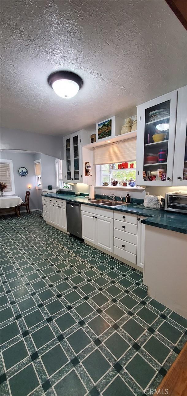 kitchen with open shelves, dark countertops, glass insert cabinets, white cabinets, and dishwasher