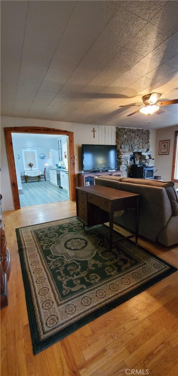 living room with hardwood / wood-style floors, a wood stove, and ceiling fan