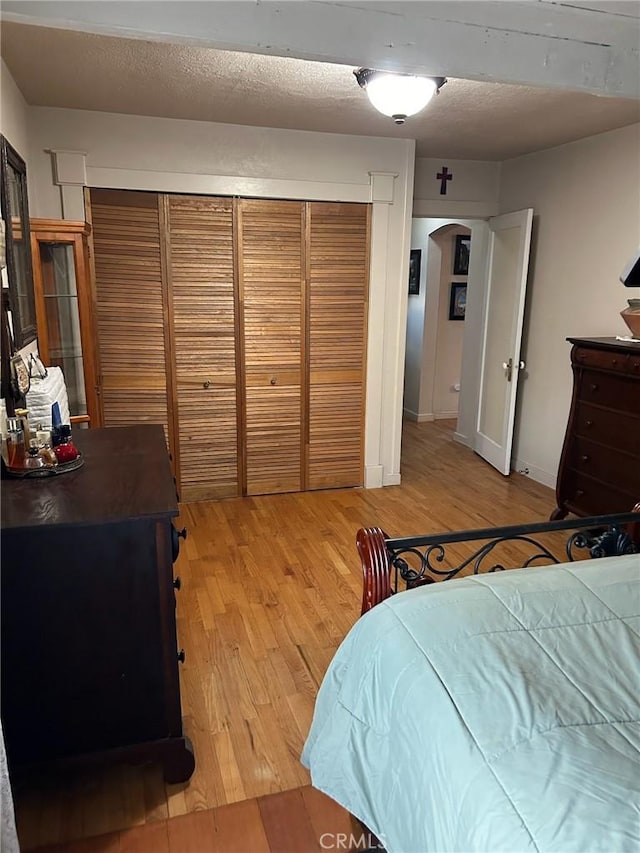 bedroom with a closet, baseboards, light wood-style flooring, and a textured ceiling