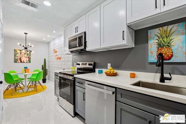 kitchen featuring appliances with stainless steel finishes, sink, a notable chandelier, white cabinetry, and hanging light fixtures