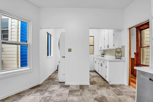 kitchen with stainless steel dishwasher, white cabinets, and stacked washer / drying machine